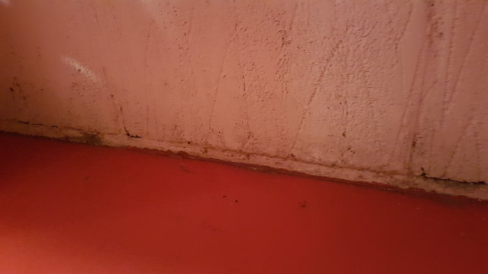 Vit vägg och röd golvskarv med synlig täcklist och tätning, utan fukt eller vatten.