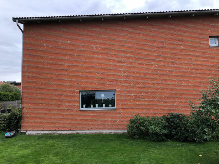 Röd tegelhusfasad med fönster och gräsmatta framför, potentiellt område för tillbyggnad.