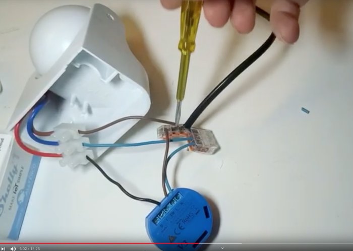 Hand som justerar trådar i en elektrisk anslutning med skruvmejsel, kopplingsklämma och rörelsevakt på bord.