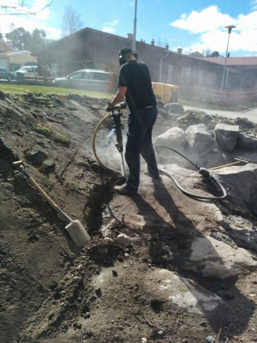 Person använder tryckluftsdriven bergborr för bergsprängning i trädgård.