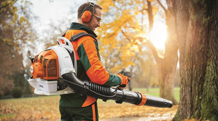 Man i arbetskläder använder en ryggburen Stihl lövblås i en solig trädgård.