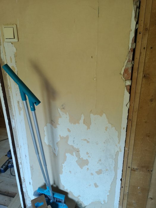 Delvis renoverad murstock med avtagande puts och synliga tegelstenar i ett sovrum under renovering.
