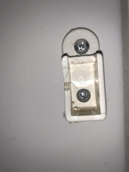 Gammal plasthållare för duschdraperiskena fastskruvad på vit kakelvägg.