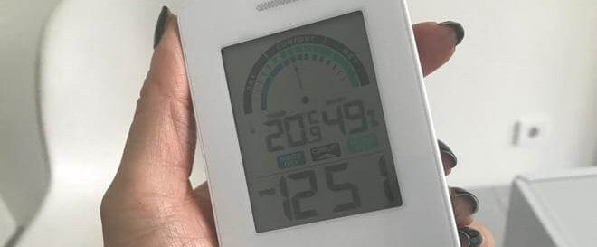 Hand håller en hygrometer som visar inomhus temperatur och luftfuktighet.