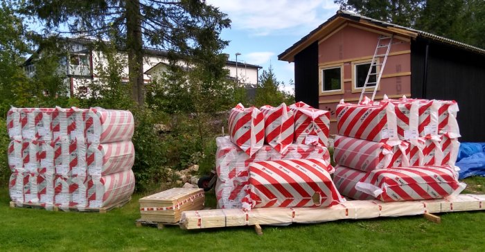 Flertal balar med isolering i olika storlekar levererade utomhus bredvid ett litet hus.