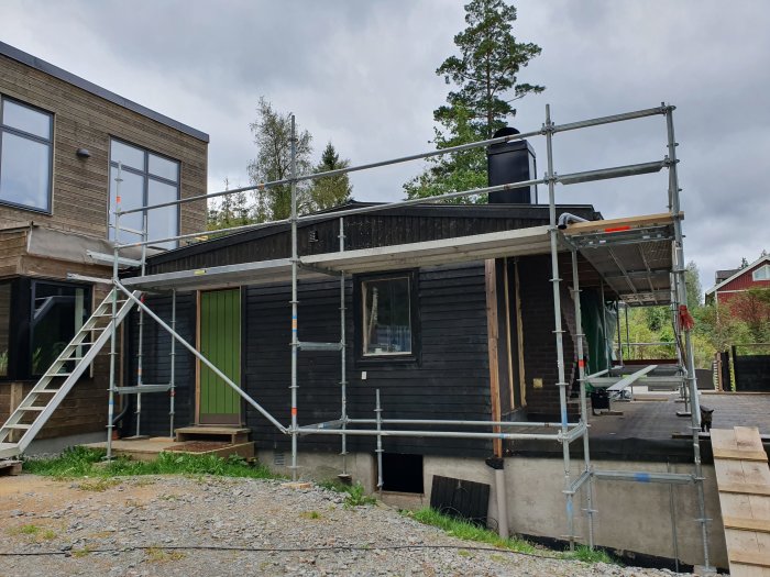 Hus med byggnadsställning och delvis riven vägg och plåttak, indikerar renovering på gång.