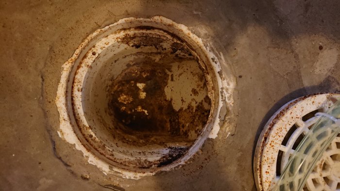Gammal rostig golvavlopp utan vattenlåsinsats i betonggolv, synligt avloppsrör.