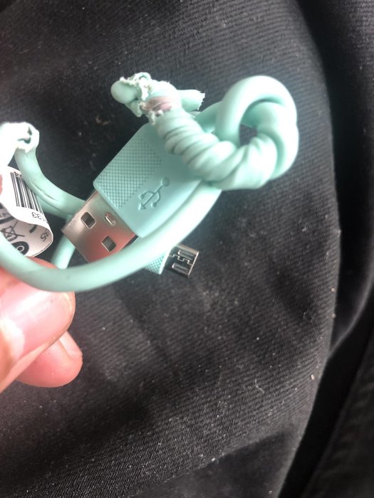 Deformerad USB-kabel som smält i tvätt och torktumling mot svart tyg.