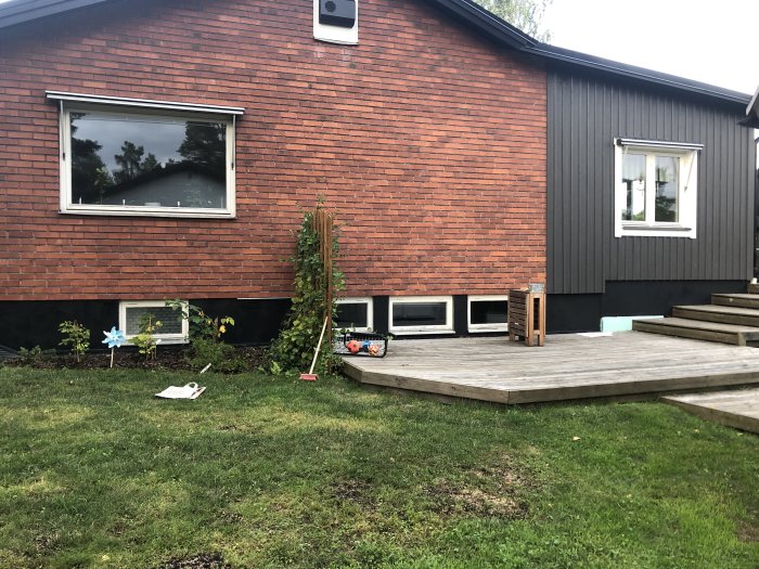 Hus med röd tegelfasad och mörkgrå vindskivor och grund, med träaltan och trädgård.