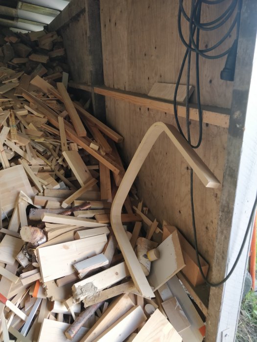 Träbit formad som en stor C-clamp på en hög med diverse träspill och avklipp i en vedbod.