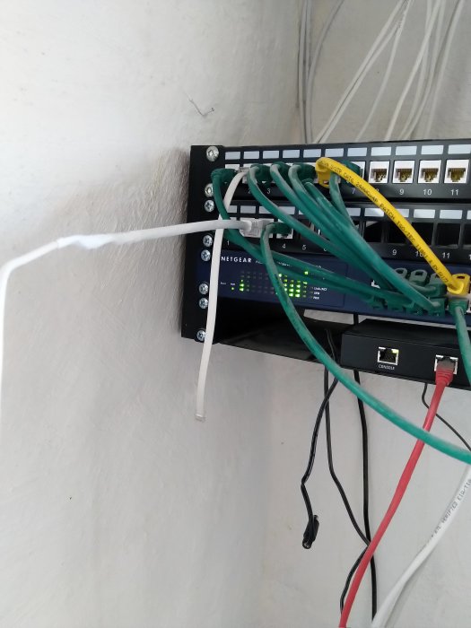 Patchpanel och nätverksutrustning med anslutna kablar, inklusive en styv installationskabel.