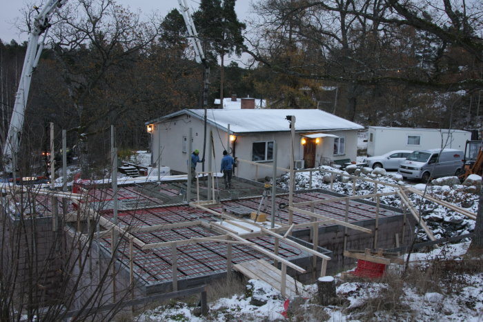 Byggarbetsplats med arbetare som förbereder för gjutning av bjälklag i vintermiljö, inklusive avloppsrör och golvvärmeinstallation.