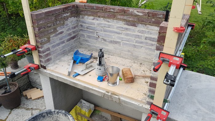Byggprojekt med Bessey K-Revo klämmor, murslev, bruk och snöre runt en halvfärdig tegelmur.