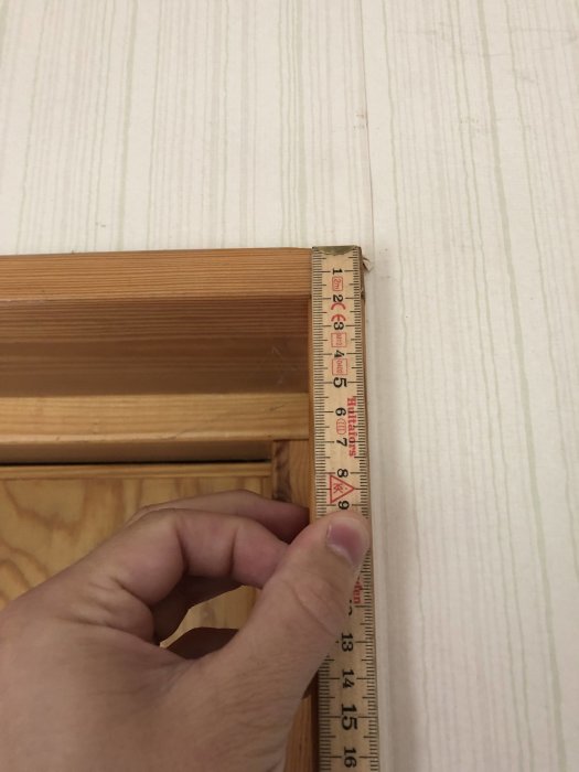 Hand håller ett måttband mot en dörrkarm för att mäta bredden på en potentiell ny ytterdörr.