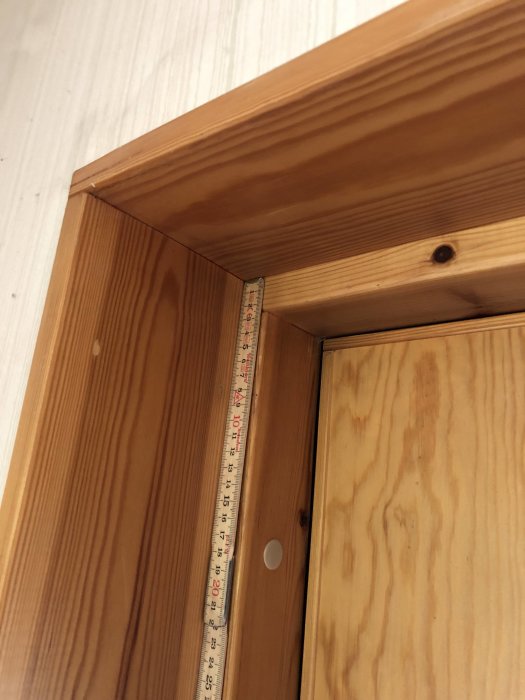 Måttband mot en träytterdörr för att mäta storleken, synlig vid dörrkarmens övre hörn.