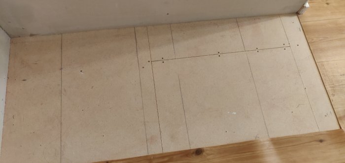 Golv med spånskivor och blyertsmarkeringar, plastmatta vid kanten avser att tas bort.