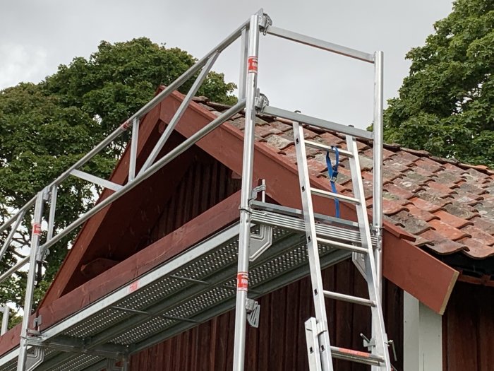 Ställning vid en röd träbyggnad under renovering av tak med tegelpannor.