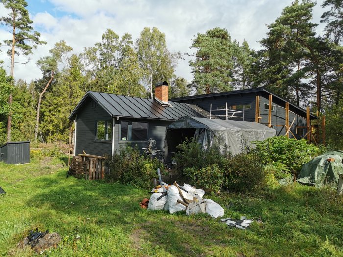 Hus under renovering med nytt bandtäckt svart tak och omgivande grönska.