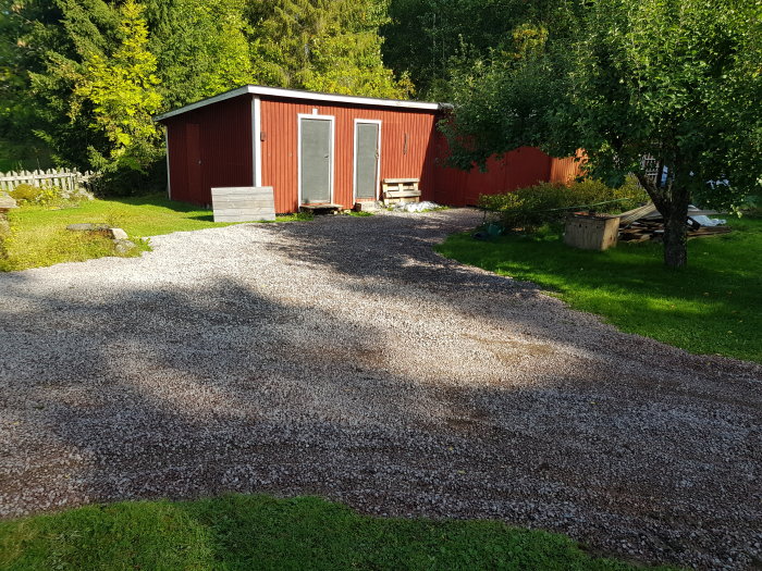 Nygrusad uppfart med makadam intill ett rött hus och grönt gräs med träd i bakgrunden.