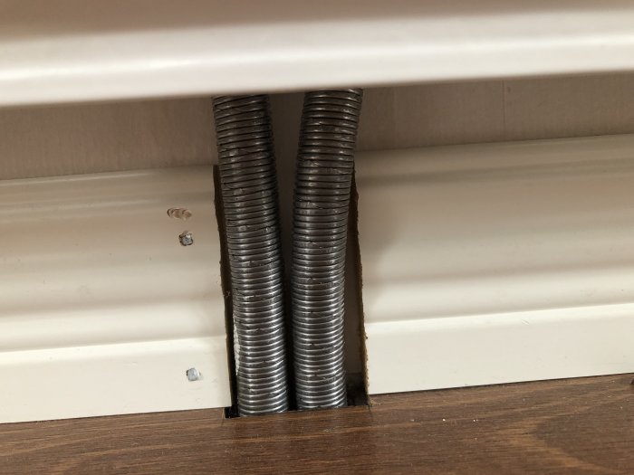 Två flexibla metallrör för element kopplade till ett hus från 1979 syns bakom en list.