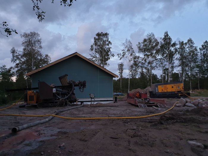 Borrigg och generator vid en pågående installation av bergvärme nära en byggnad under skymning.