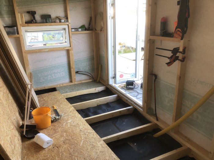 Renoveringsprojekt med isoleringsarbete, delvis lagt golv och vattenrör inomhus under konstruktion.