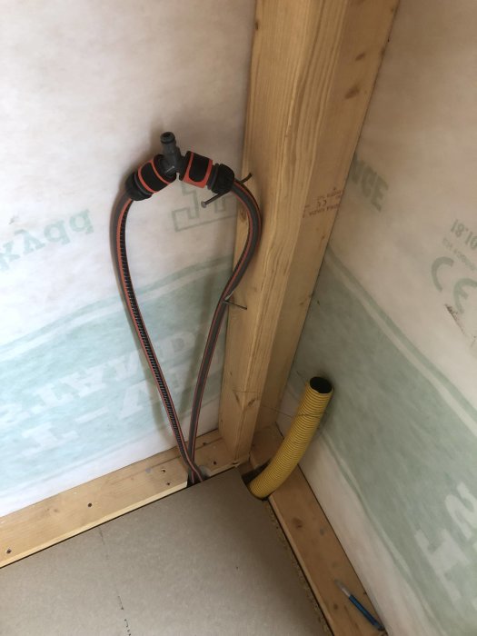 Vattenledning och elkablar installerade i vägghörn med isolering och två golvgipsplattor på plats.