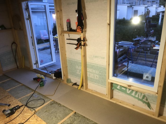 Renoveringsarbete med oslaget golv och verktyg framför isolerade väggar med fönster och dörrar.