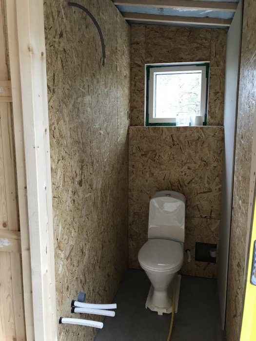 Toalett under renovering med osb-väggar, nytt fall i duschen och en nisch vid sidan av toalettstolen.