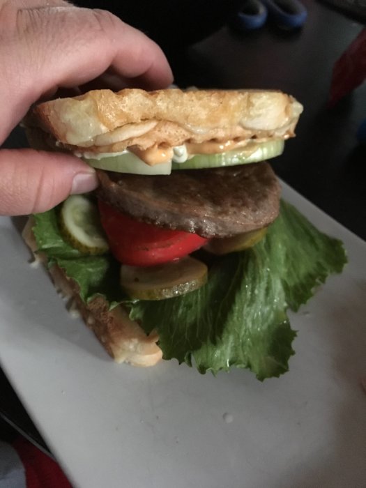 Hamburgare med rostbröd som bröd, ost, chili, sallad och tomat i en person's hand.