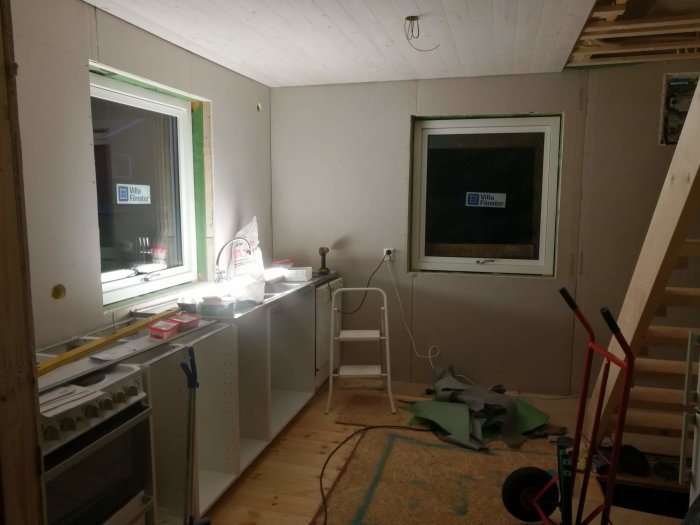 Köksrenovering med nya fönster installerade och skåpsstommar på plats i ett halvfärdigt rum.