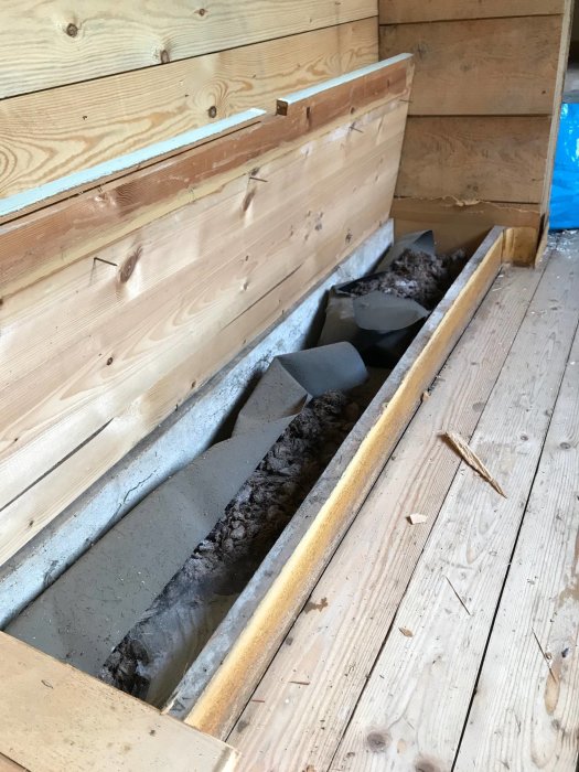 Gammalt brunt isoleringsmaterial mellan träbjälkar med tjock svart papp under, i ett hus från tidigt 1900-tal.