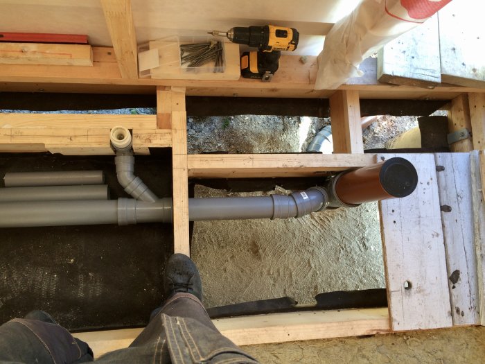 Vy från ovan på en pågående VVS-installation med gråa och bruna rör i en husgrund under konstruktion.