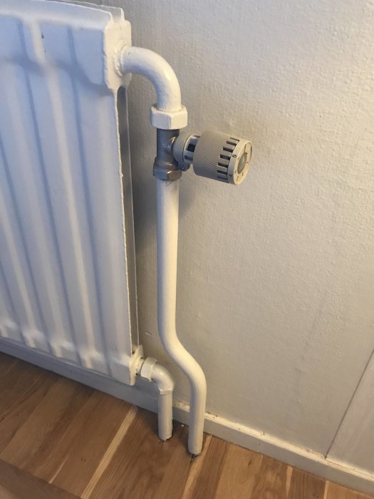 Radiator med synliga vita rör mot en vägg i behov av renovering, diskussionsämne för elementflytt.