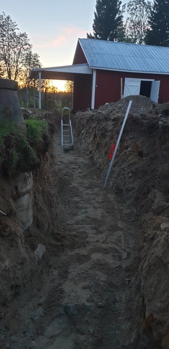 Ett djupt grävt dike nära ett rött hus vid skymning, planerat för isolering och skydd mot plogning.