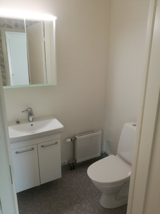 Nyrenoverat badrum med vit handfat och förvaring, toalettstol och radiator, ljus inredning.