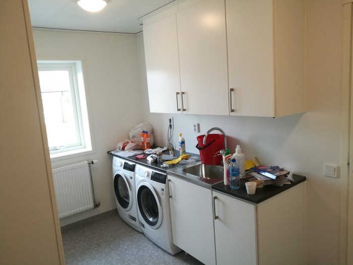 Nyrenoverat kök med vita skåp och tvättmaskiner under arbetsbänken, diverse föremål på bänken.