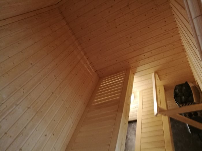 Träpaneler på interiör av sluttande tak och vägg med inbyggd garderob och hyllor.