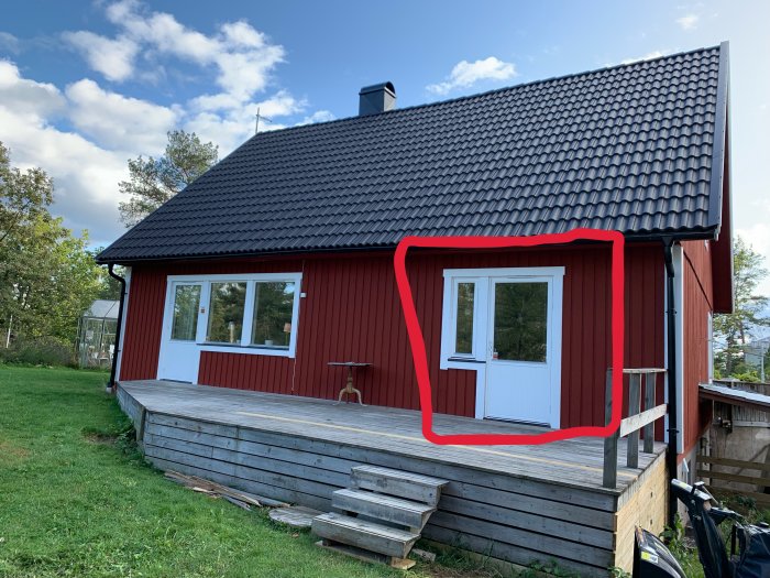 Altandörr på röd trähusfasad, rödmarkerad för att användas som vinterentredörr, omgiven av snöfri yta.