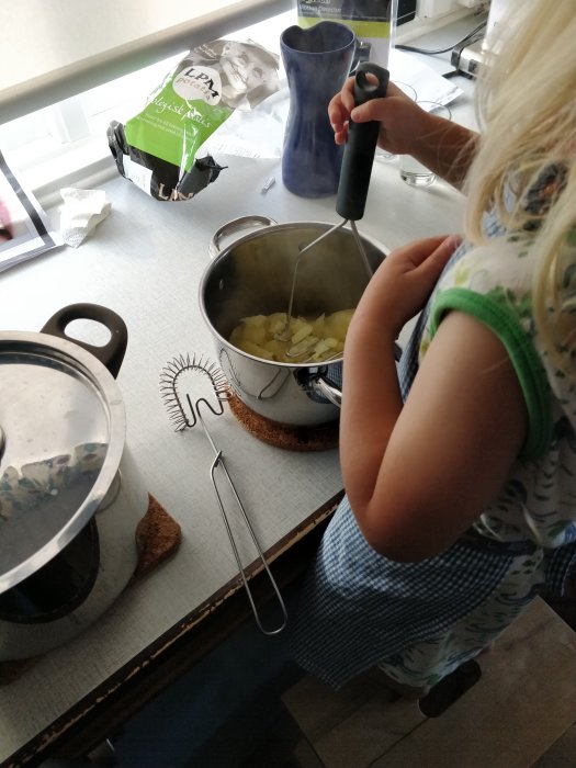 Barn gör potatismos med potatispress vid köksbänk.