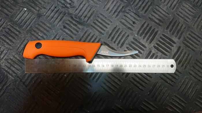 Återanvänd kniv med orange handtag bredvid en stållinjal på en diamantmönstrad yta.