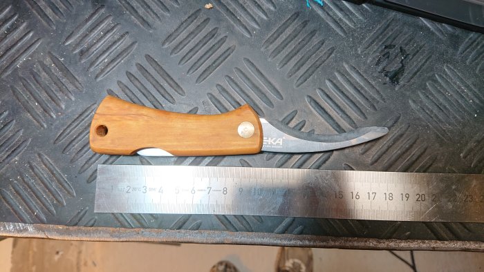 Ommakerad kniv med nytt trähandtag bredvid en metallskala, placerad på en svart strukturerad yta.