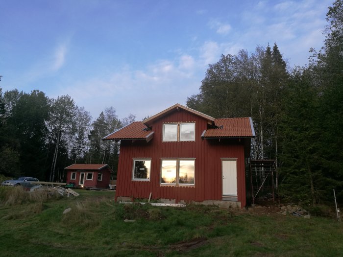 Rödmålat hus med stora fönster monterade, under en tidig kväll med spegling av solnedgången.