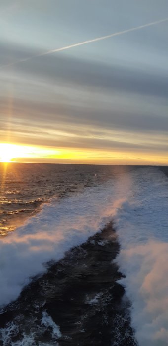 Solnedgång över havet med båtvakor och molnstrimmor på himlen.