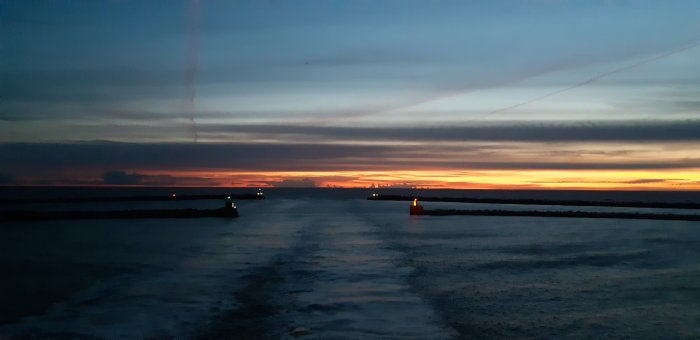 Solnedgång över havet med silhuetter av piren och navigationsljus.