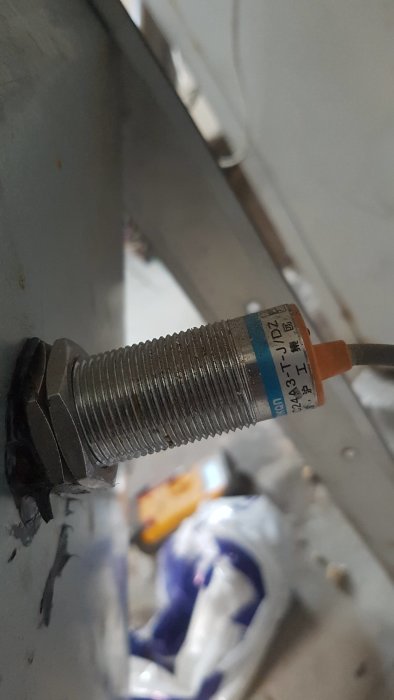 Givare från äldre pelletsanläggning monterad på metall, med kablar synliga i bakgrunden.