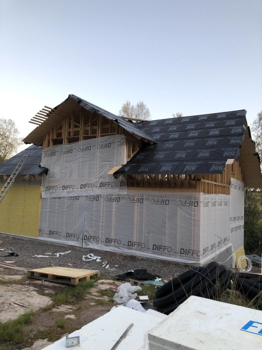 Hus under renovering med nyligen monterad vindduk och utspridda byggmaterial på marken.