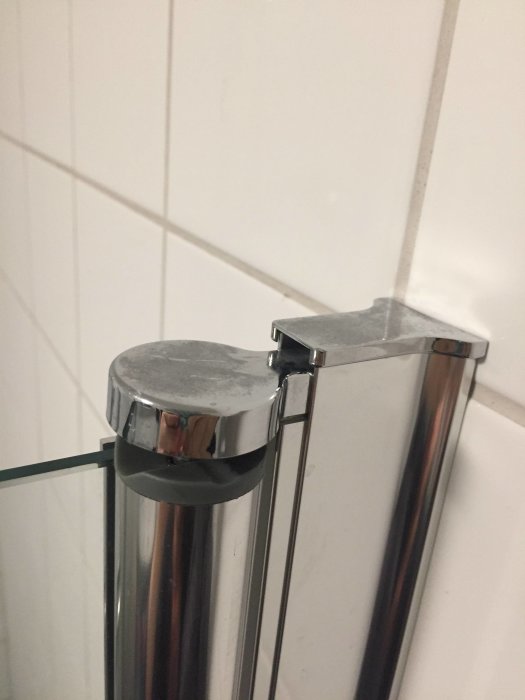 Detaljbild av en glasduschdörrs fäste mot kakelvägg där glaset möter metallstänger.