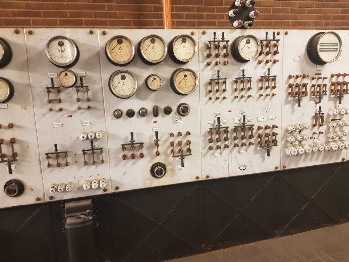 Gammal kontrollpanel med mätare, knivbrytare och emaljerade skyltar för generatorstyrning.