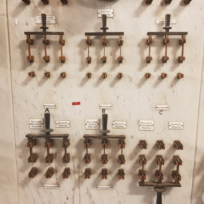 Gamla knivbrytare och kontrollinstrument monterade på en marmortavla, etiketterade för olika funktioner.
